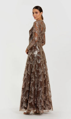 A woman wearing the Mac Duggal 69005 long formal dress—a brown, beaded sequin gown with sheer sleeves—stands against a plain white background, facing slightly to the side.
