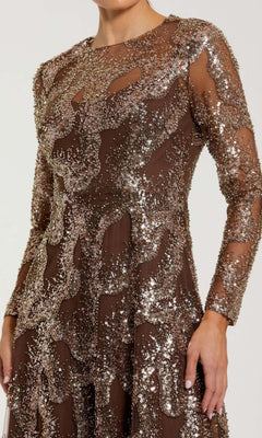Wearing the Mac Duggal 69005 long formal dress, featuring long sleeves and a sheer brown fabric adorned with intricate silver sequins and bead embellishments in decorative patterns.
