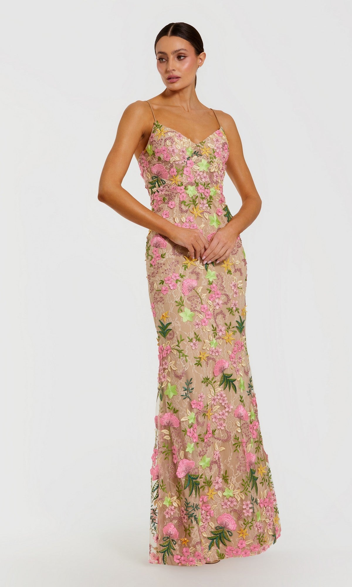 A woman wearing the Long Formal Dress: Mac Duggal 69010 in Nude Multi, a sleeveless floor-length gown with pink and green floral embroidery, stands against a plain white background.