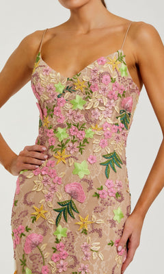A woman poses with one hand on her hip, wearing the Mac Duggal 69010 long formal dress—a sleeveless, fitted gown featuring pink, green, and yellow floral embroidery.