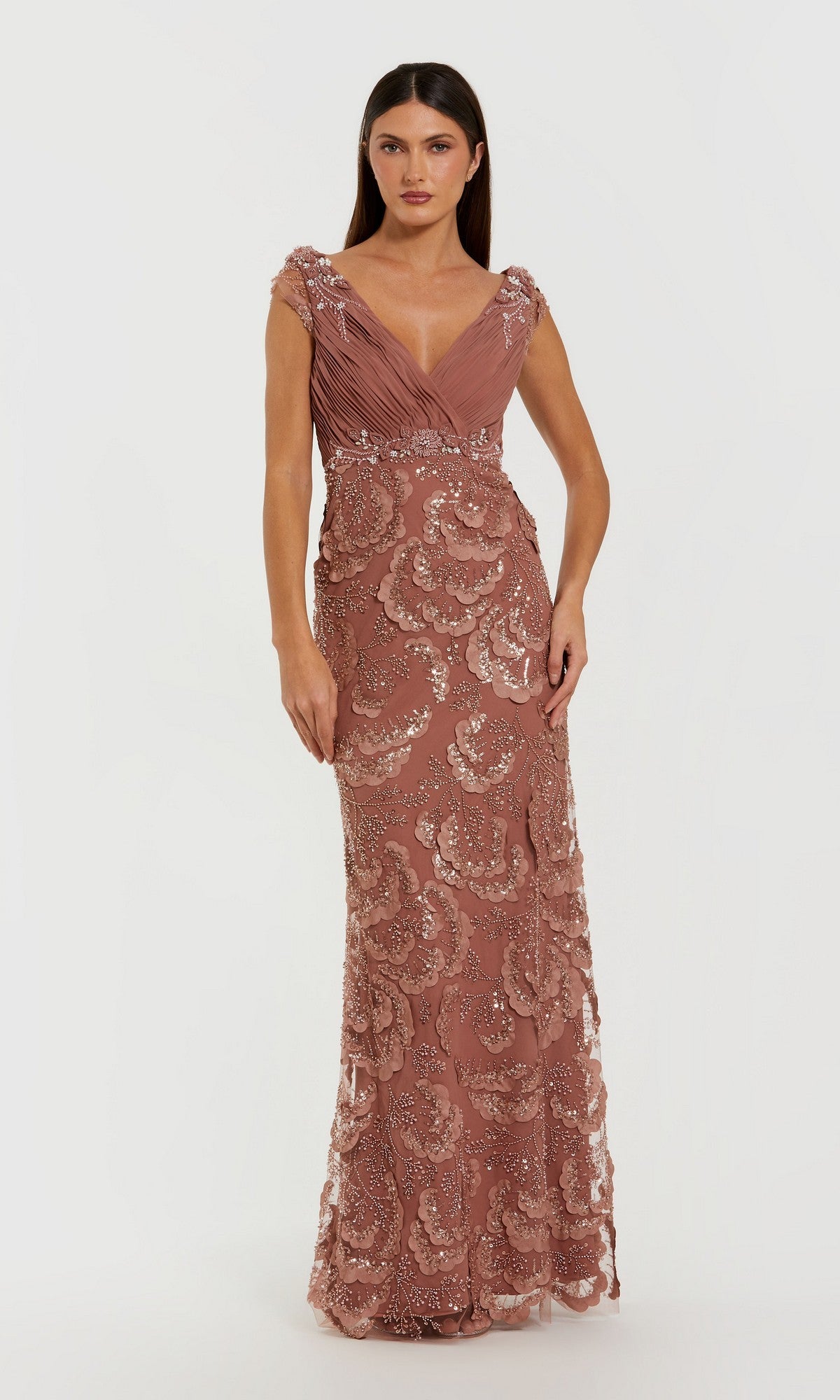 A woman wears the Mac Duggal 69022 long formal dress in rose, featuring intricate beaded floral appliqué, a pleated bodice, and embellished cap sleeves, posed against a plain white background.