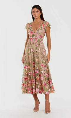 A woman wearing the Mac Duggal 69024 Tea-Length Party Dress in Nude Multi, featuring pink floral embroidery and short cap sleeves, paired with open-toe heels, stands against a plain background.