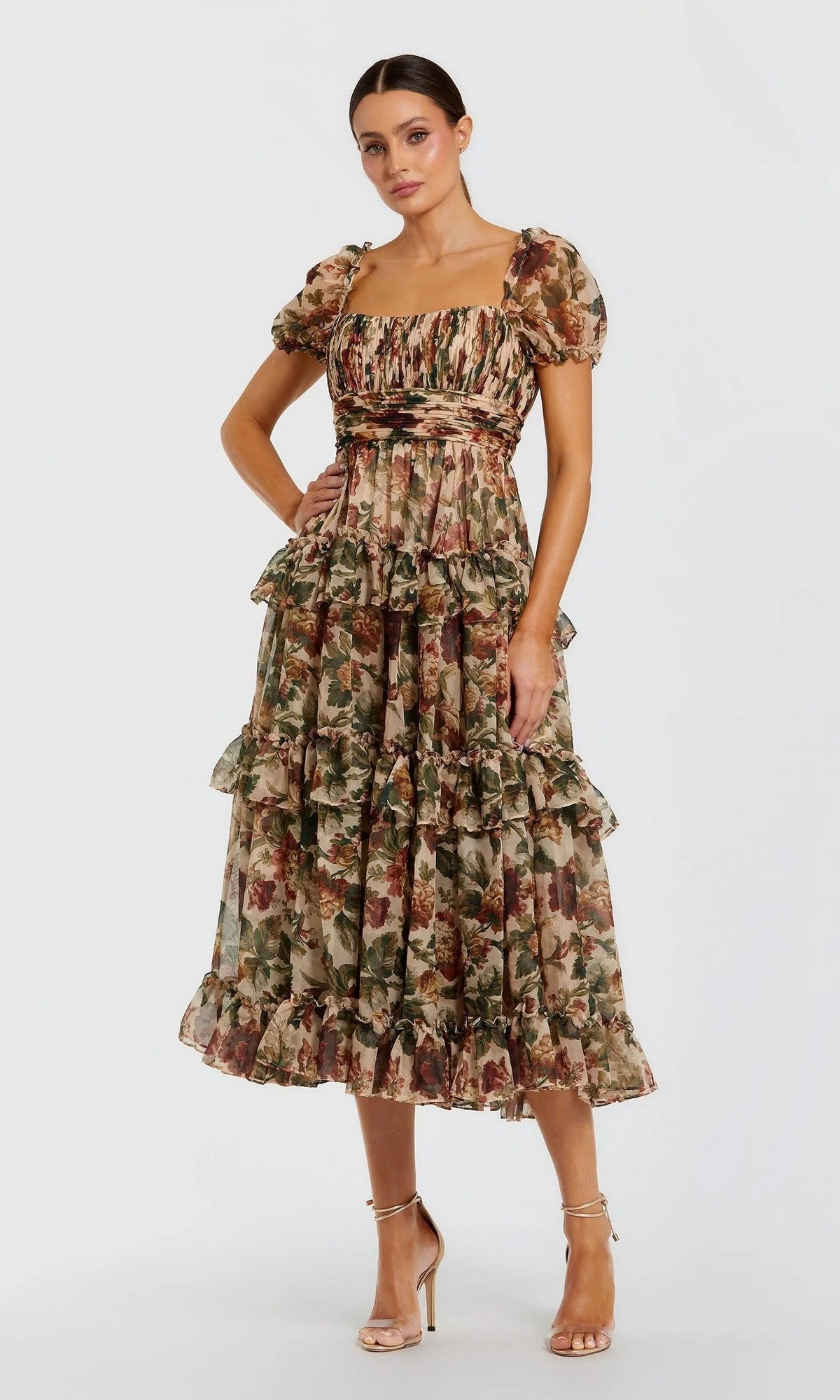 A woman models the Mac Duggal 69029 Floral Wedding-Guest Dress in Cream Multi, featuring puff sleeves, floral print, and ruffles, paired with strappy heels against a plain white background.