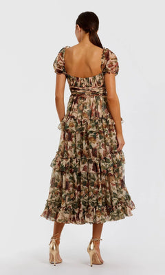 A woman faces away in the Mac Duggal 69029 Floral Wedding-Guest Dress, featuring ruffled puff sleeves and a square neckline, styled with metallic gold heels—an ideal choice for wedding guests.