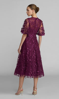 Woman in profile wears the Mac Duggal 69036 Lace Midi Wedding Guest Dress—short sleeves, purple floral lace—set against a plain backdrop. Ideal for wedding guests.