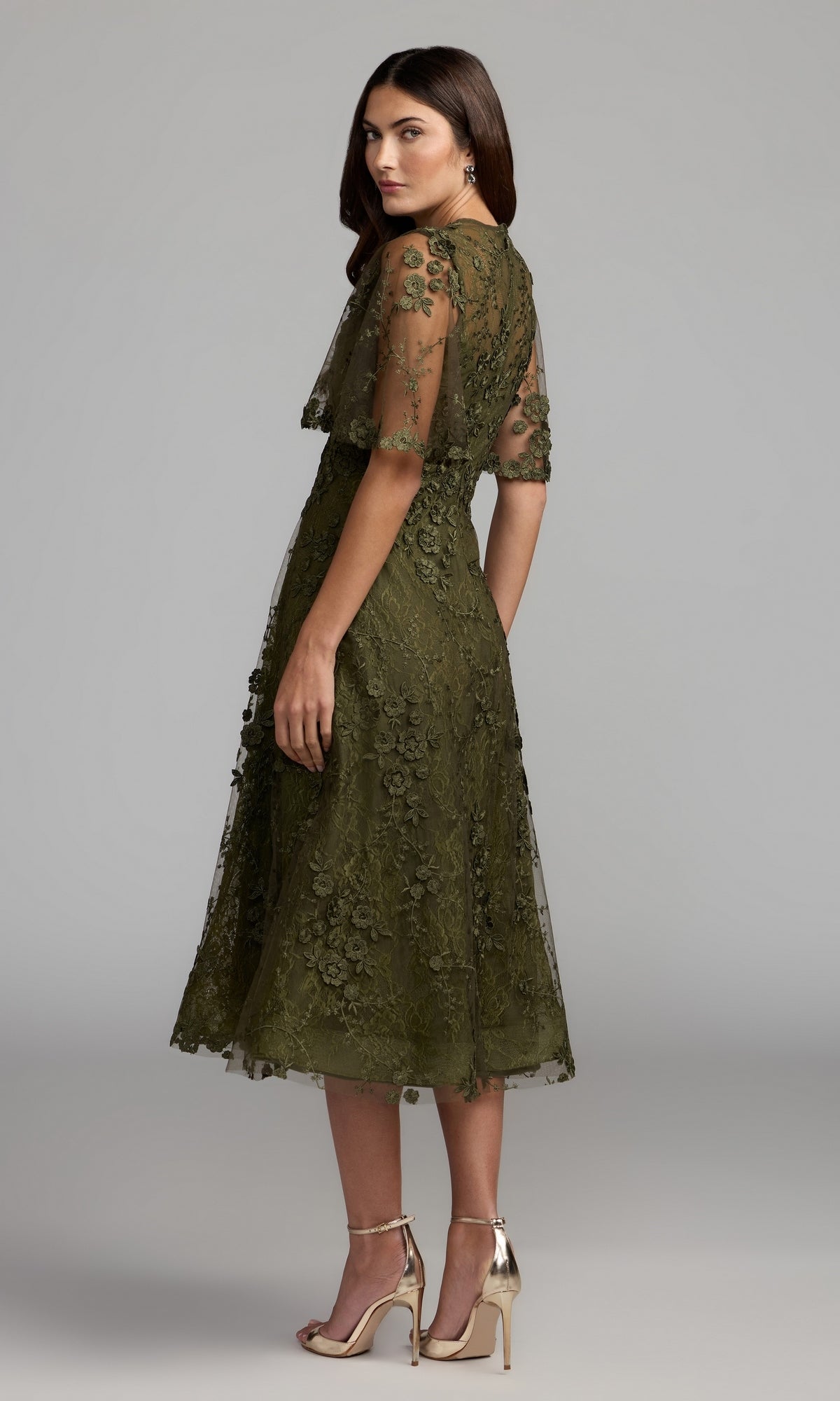 Woman wearing the Lace Midi Wedding Guest Dress: Mac Duggal 69036—a knee-length, olive green short sleeve lace midi dress—paired with metallic high-heeled sandals and standing against a plain gray background; a chic choice for any wedding guest.