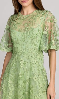 Woman wearing the Mac Duggal 69036 Lace Midi Wedding Guest Dress in light green, featuring short sleeves, floral embroidery, and sheer detailing—shown head to mid-thigh—a stunning choice for wedding guests.
