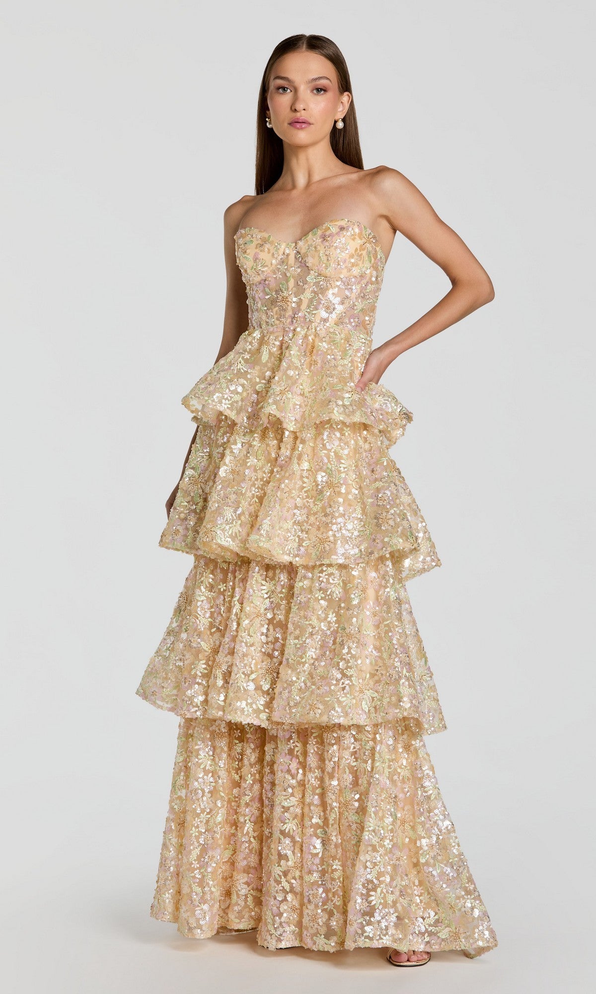 A woman wearing the Mac Duggal 69044 long formal dress in Nude Multi, which features a strapless design, tiered floor-length silhouette, and gold and silver sequin embellishments, poses against a plain light background.