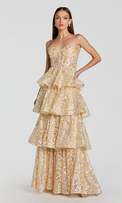 A woman wearing the Mac Duggal 69044 long formal dress in Nude Multi, which features a strapless design, tiered floor-length silhouette, and gold and silver sequin embellishments, poses against a plain light background.