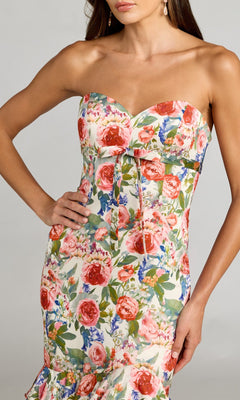 A woman models the Mac Duggal 69059 Long Formal Dress, a strapless design adorned with pink and red floral patterns. The dress features a fitted bodice, a delicate bow accent at the waist, and hints at an elegant mermaid silhouette in this upper-body view.