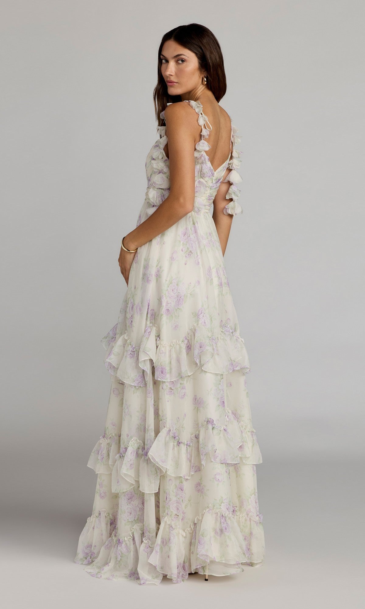 A woman stands sideways against a plain background, looking over her shoulder while wearing the Mac Duggal 69061 long formal dress featuring ruffles, an A-line silhouette, and a V-back.