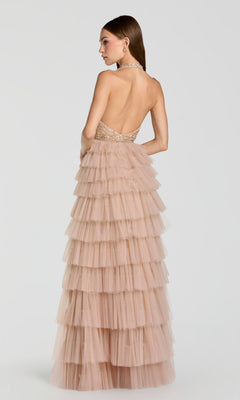 A woman stands against a plain light background, facing away from the camera, wearing the Mac Duggal 69062 long formal dress—a backless and strapless layered blush pink tulle gown with a fitted bodice.