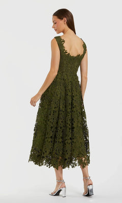 A woman stands on a plain light background in silver high-heeled sandals, wearing the Midi Party Dress: Mac Duggal 69073—a sleeveless, green floral lace A-line midi dress with a scalloped hem that exudes sophistication and charm.