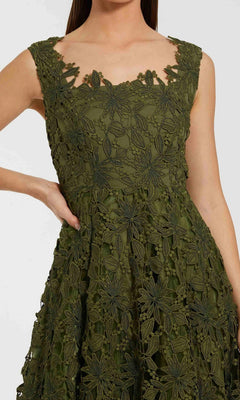 A woman models the Mac Duggal 69073 Midi Party Dress, a sleeveless olive green A-line dress featuring an intricate floral lace overlay; she is posed from shoulder to knee with one hand resting on her hip.