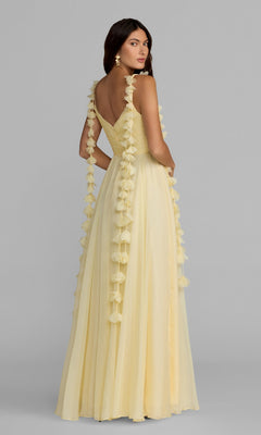 Wearing the Mac Duggal 69086 long formal dress—an A-line, pale yellow gown featuring floral detailing on the shoulder straps—a woman stands gracefully, looking over her shoulder against a plain gray background.