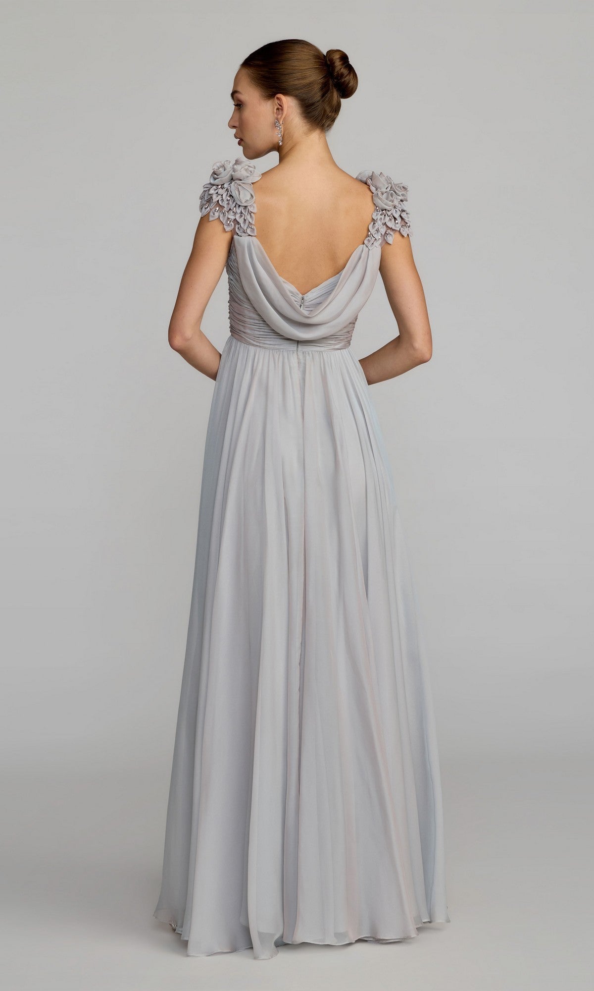 A woman stands against a plain background wearing the Long Formal Dress: Mac Duggal 69088, a light gray gown with an elegant A-line silhouette, draped back, ruffled short sleeves, and her hair styled in a neat bun.