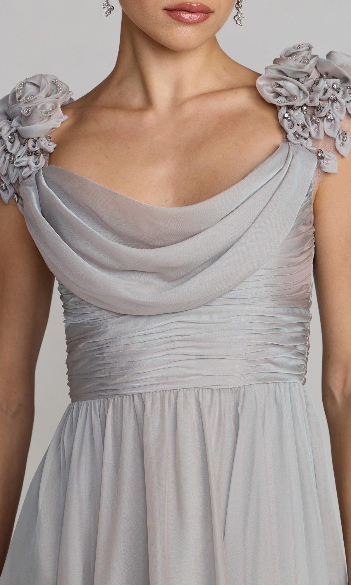 A woman wearing the Mac Duggal 69088 long formal dress in light gray, featuring a ruched chiffon design, draped neckline, and embellished floral shoulder details.