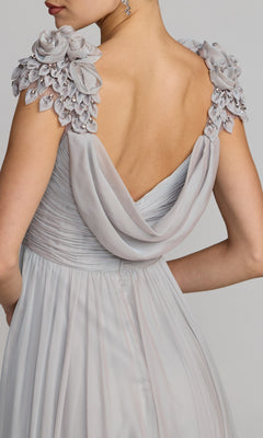 A woman photographed from behind wears the Mac Duggal 69088 long formal dress in light gray, featuring a draped back and floral embellishments on the shoulders.