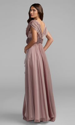 A woman models the Mac Duggal 69089 long formal dress in mauve chiffon, featuring draped sleeves and a crystal-embellished waistband, as she stands against a plain gray background and faces slightly away from the camera.