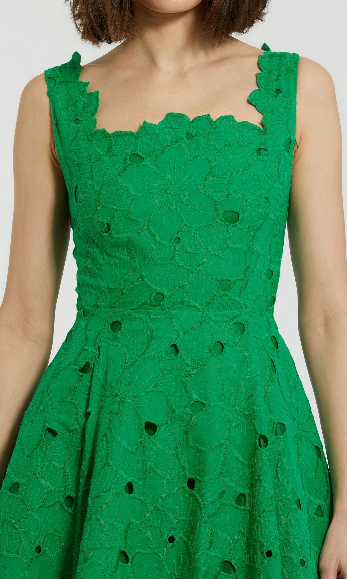 A woman wearing the Mac Duggal 69096 Midi Party Dress—a sleeveless green dress featuring a floral textured pattern and cutout details.