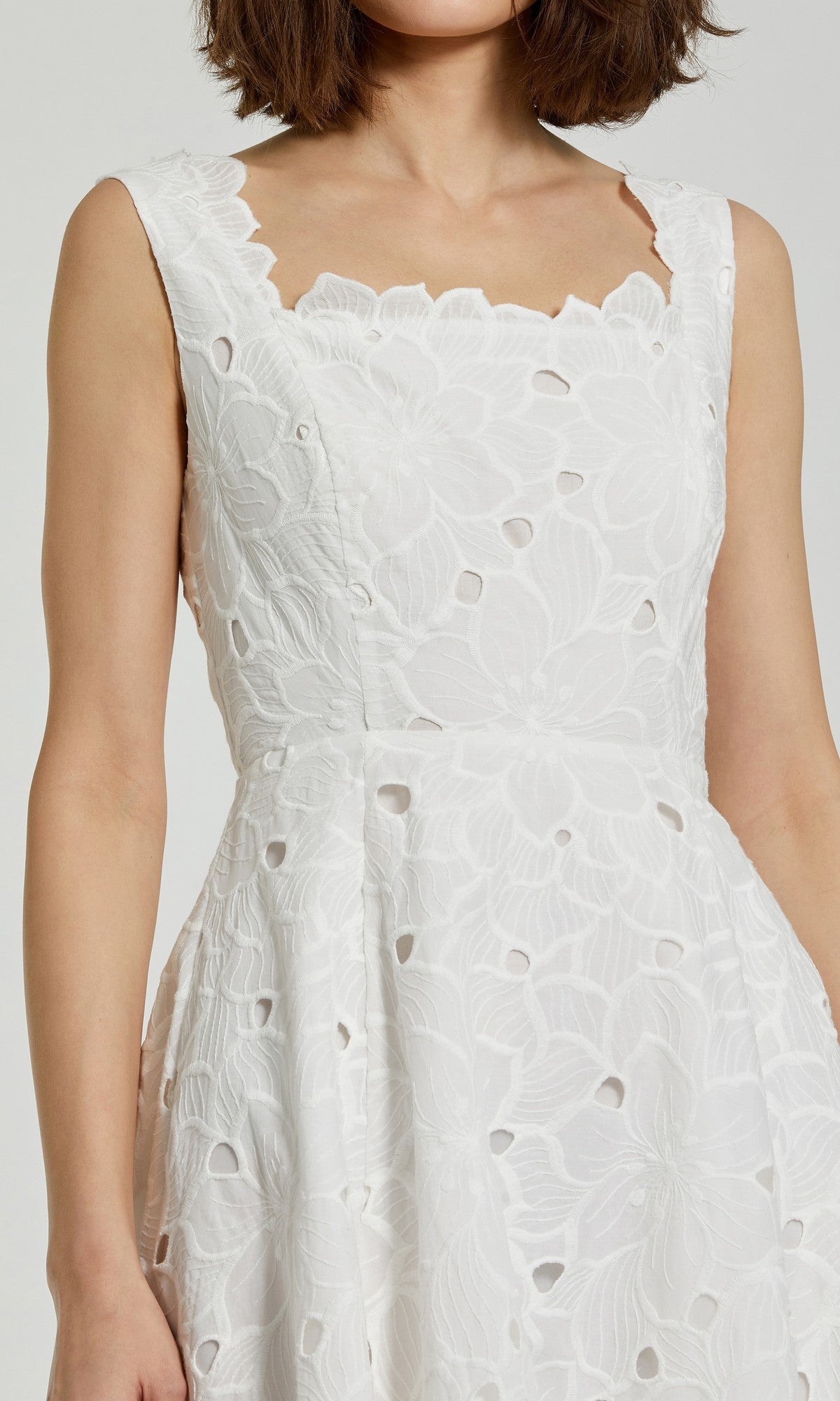 A woman wearing the Mac Duggal 69096 Midi Party Dress, a sleeveless white dress with floral embroidery and cutout details, shown from shoulders to waist.