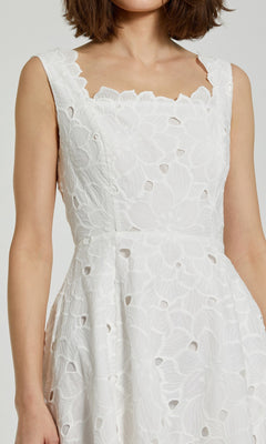A woman wearing the Mac Duggal 69096 Midi Party Dress, a sleeveless white dress with floral embroidery and cutout details, shown from shoulders to waist.
