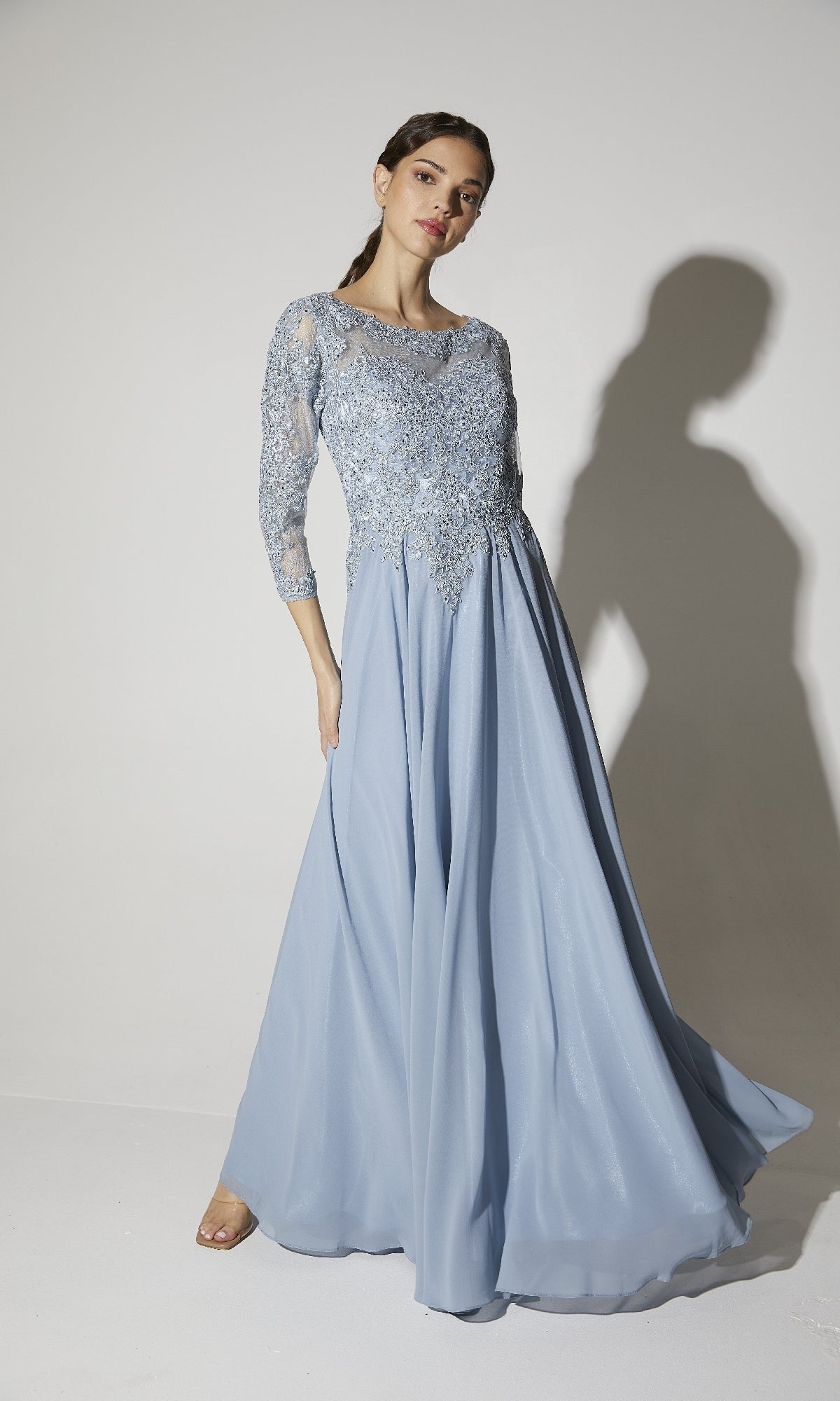 A woman models the Eureka 6909, a long-sleeve formal dress with a lace bodice and flowing light blue A-line skirt, set against a plain background.