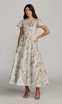 A woman wearing the Mac Duggal 69107 Tea-Length Party Dress in Oyster Multi—a modest, short-sleeved, sequin floral dress—paired with silver high-heeled sandals, standing against a plain background.
