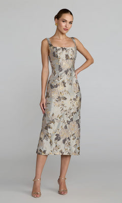 A woman stands in the Mac Duggal 69152 Floral Midi Wedding Guest Dress in Platinum Multi—a sleeveless, floral-patterned midi dress with a square neckline—styled with strappy heels and earrings against a plain background.