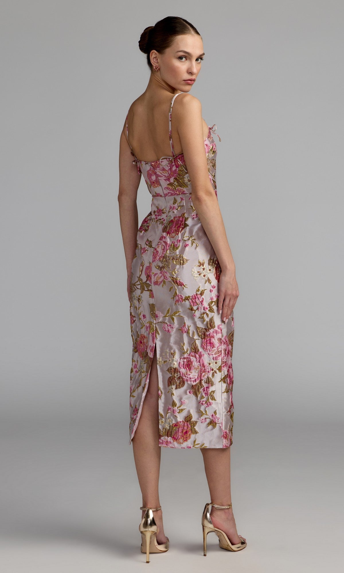 A woman stands in heels against a studio backdrop, facing away from the camera and wearing the Mac Duggal 69153 midi party dress—a sleeveless design with a floral-brocade silhouette and a chic slit.