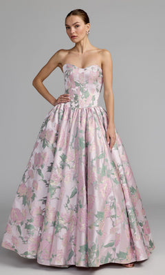 A woman poses against a plain gray background wearing the Mac Duggal 69162 long formal dress in Pink Multi, a strapless ball gown with a full skirt and an eye-catching metallic floral print in pink and green shades.