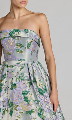 A woman wears the Mac Duggal 69172 Long Formal Dress—a strapless floral ballgown shimmering in silver, adorned with a delicate pattern of green, lavender, and gold flowers—standing against a plain background.