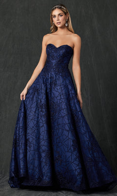 A woman stands against a dark textured background wearing the Juliet 692 long prom dress, featuring a strapless, sweetheart neckline and floor-length navy blue fabric adorned with intricate beaded patterns.