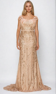 A woman stands wearing the Cinderella Couture 8057J, a floor-length fitted blush prom dress with gold sequins, beading, cap sleeves, and a sheer neckline.