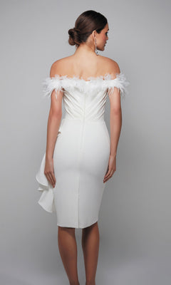 A woman in the Alyce 70000 knee length semi-formal dress, featuring off-the-shoulder white fabric with feather trim, stands facing away with her hair in a low bun.