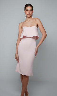 A woman modeling the Knee Length Semi-Formal Dress: Alyce 70002 in Rosewater, featuring a strapless design and ruffled overlay, stands against a plain gray background.