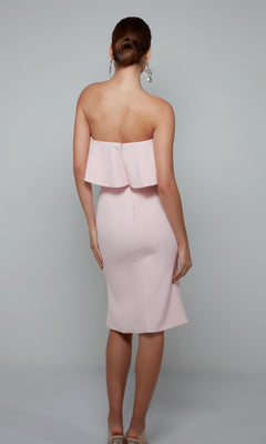 A woman with her hair in a bun, wearing dangling earrings, faces away in the Alyce 70002 knee-length semi-formal dress in light pink.