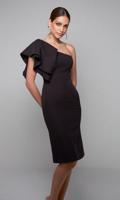 A woman wears the Alyce 70005 knee-length semi-formal dress, featuring a fitted, one-shoulder design with a ruffled sleeve, against a plain light gray background.