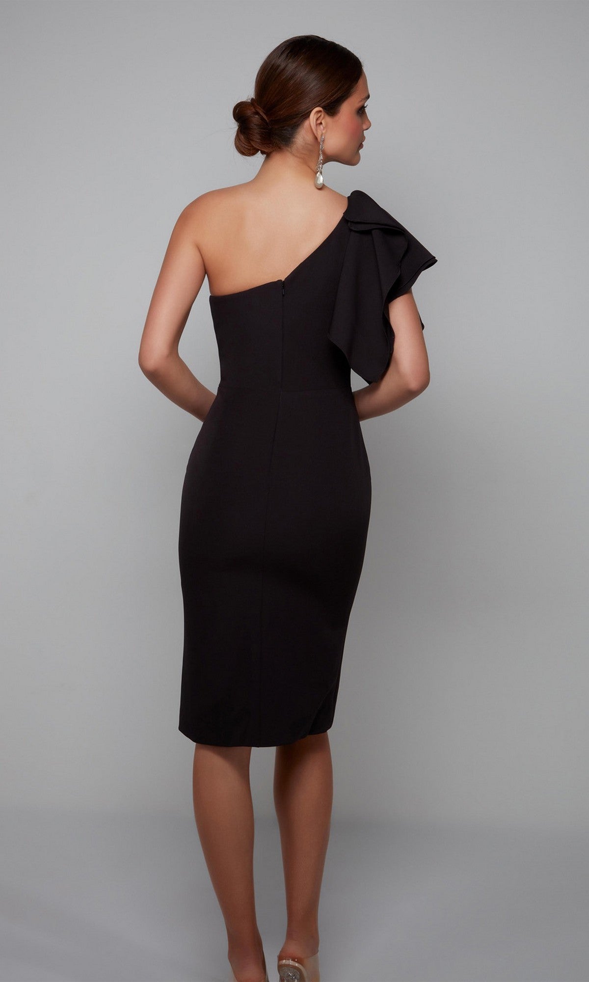 A woman models the Alyce 70005 knee-length semi-formal dress, featuring a black one-shoulder design with a large ruffle detail, against a plain gray background, facing away from the camera.