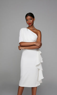 A woman poses with arms crossed, wearing the Knee Length Semi-Formal Dress: Alyce 70006, featuring a one-shoulder design and ruffle detail on the skirt, against a plain grey background.