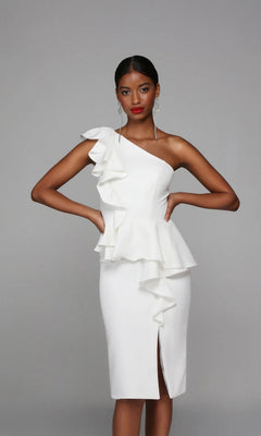A woman stands against a plain grey background wearing the Alyce 70007: a knee-length white party dress featuring an elegant one-shoulder ruffle sheath design with a front slit.