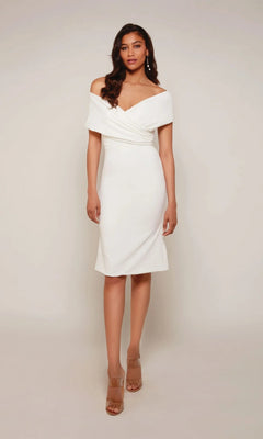 A woman stands against a plain background wearing an ivory Knee Length White Party Dress: Alyce 70023 and nude open-toe heels.