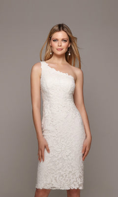 A woman wears the Alyce 70029 Knee Length White Party Dress with a fitted silhouette and sequin lace details, standing against a plain gray background.