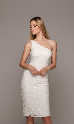 A woman stands against a neutral background wearing the Knee Length White Party Dress: Alyce 70029—a stylish one-shoulder lace dress perfect for any cocktail event.