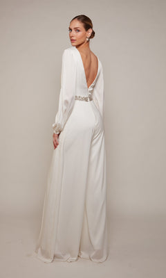A woman models the Alyce 70031 Long Formal Jumpsuit—a white, floor-length, long-sleeved satin-chiffon style featuring an open back and a decorative waistband—posed against a light background.