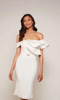 A woman wears the ivory Knee Length White Party Dress: Alyce 70032, featuring an off-the-shoulder design, ruffle details, and a small brooch at the waist.