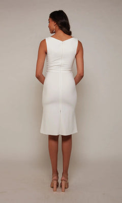 A woman faces away, wearing the Alyce 70037 knee-length white party dress with nude heels, set against a plain light background.