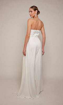 A woman wearing the Alyce 70050 Long Formal Jumpsuit, featuring a strapless fitted bodice and flowing skirt, stands against a plain light background, facing slightly away from the camera.