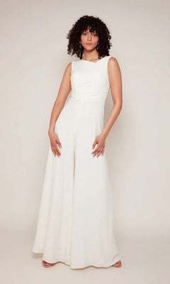 A person stands against a plain background wearing the Alyce 70052 Long White Jumpsuit in Diamond White—sleeveless and wide-leg—paired with open-toed shoes.