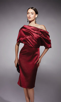 A woman wearing the Knee Length Semi-Formal Dress: Alyce 70060, an off-the-shoulder, shiny cocktail dress with short sleeves, styled with a black clutch and dangling earrings.